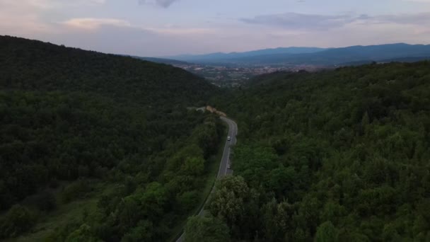 緑と風景輸送と旅行に囲まれたセルビアの曲がりくねった道に沿って運転夏の夜の車の中で山の範囲上の曲技アスファルト道路の空中ドローン映像 — ストック動画