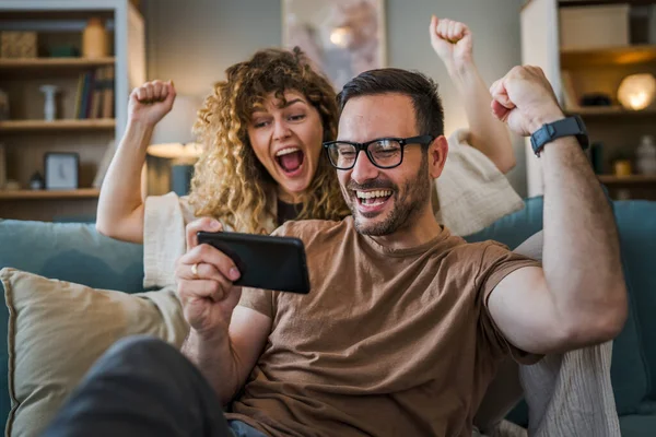 Adult couple man and woman caucasian husband and wife or boyfriend and girlfriend he play video games at home hold mobile phone smart phone have fun leisure joy and bonding concept copy space