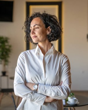 Yetişkin bir kadın Kafkas kadın iş kadını iş yerinde ya da evde duruyor gerçek insanlar yer kopyalıyor beyaz gömlek kıvırcık saçlar giyiyor