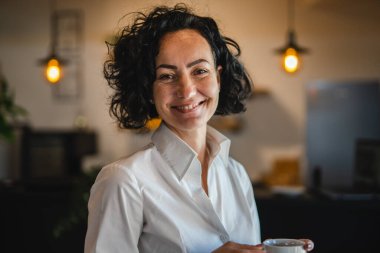 Yetişkin bir kadın Kafkas kadın iş kadını iş yerinde ya da evde duruyor gerçek insanlar yer kopyalıyor beyaz gömlek kıvırcık saçlar giyiyor