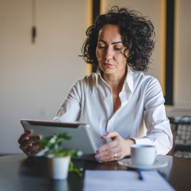 Bir kadın işkadını kafeteryada ya da restoran yöneticisinin masasında oturuyor. İş yerinde dijital tablet kullanıyor. İş yapan yetişkin bir kadın girişimci.