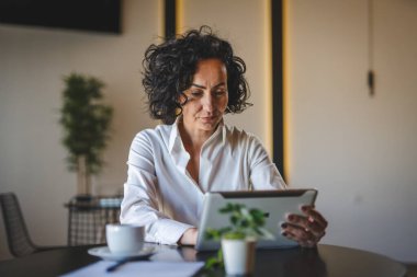 Bir kadın işkadını kafeteryada ya da restoran yöneticisinin masasında oturuyor. İş yerinde dijital tablet kullanıyor. İş yapan yetişkin bir kadın girişimci.