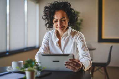Bir kadın işkadını kafeteryada ya da restoran yöneticisinin masasında oturuyor. İş yerinde dijital tablet kullanıyor. İş yapan yetişkin bir kadın girişimci.