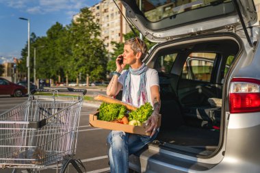 Yetişkin beyaz bir kadın, alışveriş merkezinin otoparkında arabasının bagajında ya da sebze dolu bir markette arabasının bagajına koyar.