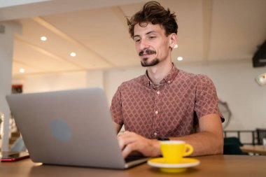 One adult modern man caucasian male with beard and mustaches wear causal shirt working remote from cafe freelance work or blog checking online content or browsing internet while sitting alone