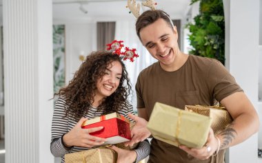 Erkek arkadaşı ya da kocası mutlu bir şekilde gülümserken elinde hediye kutusuyla evde dikilen beyaz kadın gerçek insanlar sürpriz aşk kavramını kutluyor.