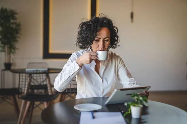 ある女性実業家はカフェやレストランのマネージャーでテーブルに座って仕事でデジタルタブレットを使用成熟した女性起業家ビジネスをオンラインで行う実際の人々はスペースをコピー — ストック写真