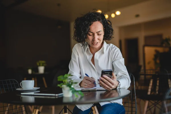 1人の女性ビジネス女性はカフェやレストランのマネージャーでテーブルに座る仕事でスマートフォンの携帯電話を使用成熟した女性起業家ビジネスをオンラインで行う実際の人がスペースをコピー書き込み — ストック写真