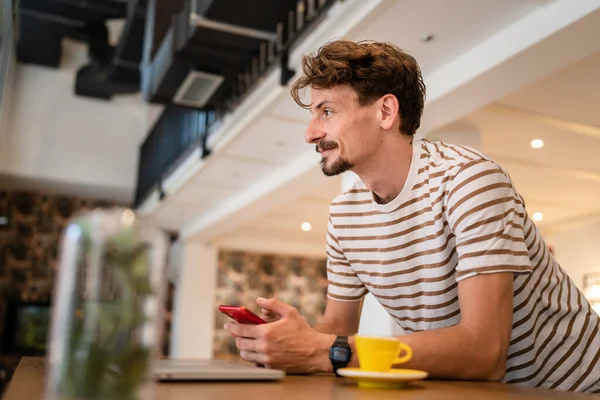 Stock image one caucasian man young adult millennial male using mobile phone stand at table in cafe at the table alone happy smile confident having online chat using internet for text messages or social network