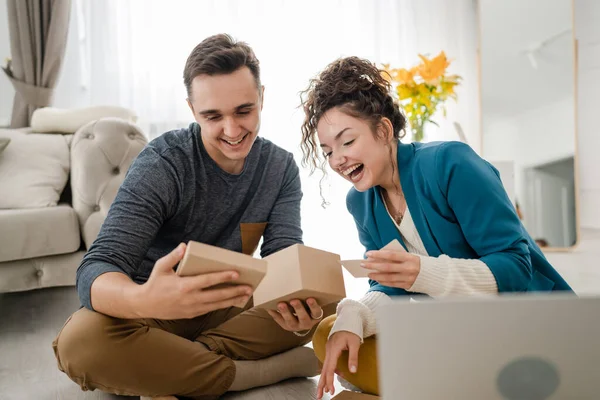 年轻的高加索夫妇的妻子和丈夫或女朋友和男朋友在家里笔记本电脑前打开礼品盒礼物和读卡机 在网上有视频叫快乐复制空间 — 图库照片
