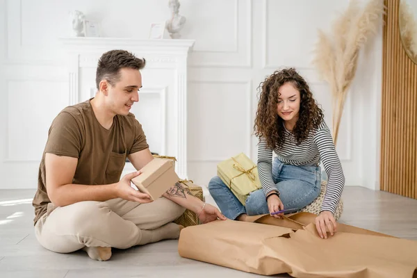 男人和女人用包装纸为朋友准备礼物 男人和女人用包装纸为朋友包装礼物 快乐的微笑在家里拿着礼品盒真实的人抄袭空间 — 图库照片