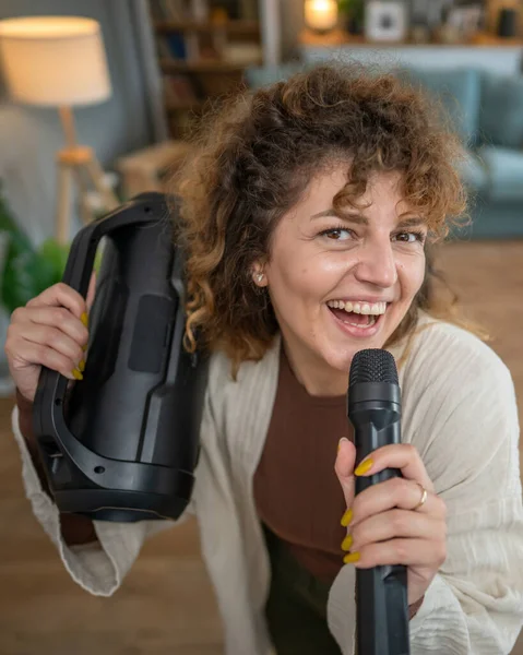 一个年轻的女人拿着话筒在家里开心地笑着唱着舞 — 图库照片