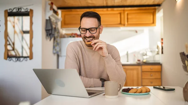 一位成年的高加索男子坐在家中餐桌旁 用手提电脑吃早饭 准备每天早上的日常工作 — 图库照片