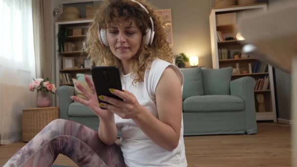 年轻女子在耳机上听音乐 准备在家接受训练 — 图库视频影像