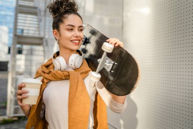 Genç bir kadın, beyaz tenli genç, dışarıda, omuzunda kaykayıyla mutlu bir portre çiziyor. Kendine güvenen gerçek bir insan, uzayı kopyalıyor.