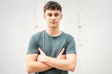 Genç, yetişkin, beyaz bir genç, dışarıda kameraya bakarak poz veriyor. Mutlu, kendine güvenen, sıradan bir gömlek giyiyor.