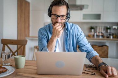 Kafkasyalı bir erkek, evinde kulaklıkla bilgisayar destekçisi olarak çalışıyor.