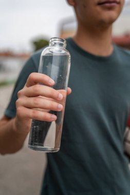 Güneşli bir günde basketbol oynarken, bilinmeyen beyaz bir gencin ellerinde açık plastik bir şişe su.