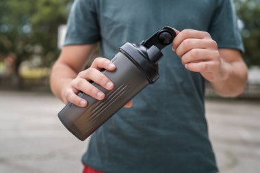 Güneşli bir günde, kimliği belirsiz beyaz bir gencin ellerinde açık plastik bir şişe su.