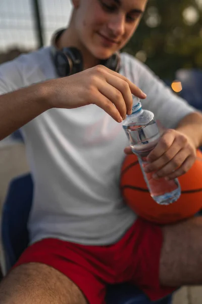 バスケットボールとスポーツをする晴れた日の屋外の未知の慎重な男の開いたプラスチックびんの手の真ん中に近づいて下さい — ストック写真