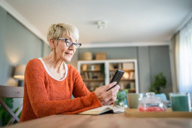 Yetişkin bir Kafkasyalı kadın evde cep telefonu akıllı telefonu kullanıyor.