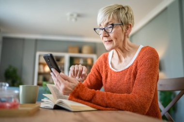 Yetişkin bir Kafkasyalı kadın evde cep telefonu akıllı telefonu kullanıyor.