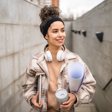 Genç bir kadın yetişkin kız öğrenci sınıfa gider dizüstü bilgisayarlı bir fincan kahve ve iş malzemesi taşır. Gerçek insan utangaç, mutlu, kulaklıklı, kendine güvenen bir gülümseme.