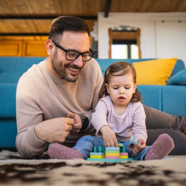 Baba ve kızı evde yerde oynuyorlar olgun yetişkin beyaz adam iki yaşındaki küçük kızıyla oynuyor ebeveynlik yaparak ve aile zamanı konseptini kopyalayarak eğleniyor gerçek insanları taklit ediyor.