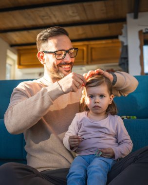 Baba ve kızı evde yerde oynuyor yetişkin beyaz bir adam iki yaşındaki küçük kızıyla oynuyor. Saçlarını yaptırıyor ve aile zamanı konseptini kopyalıyor.