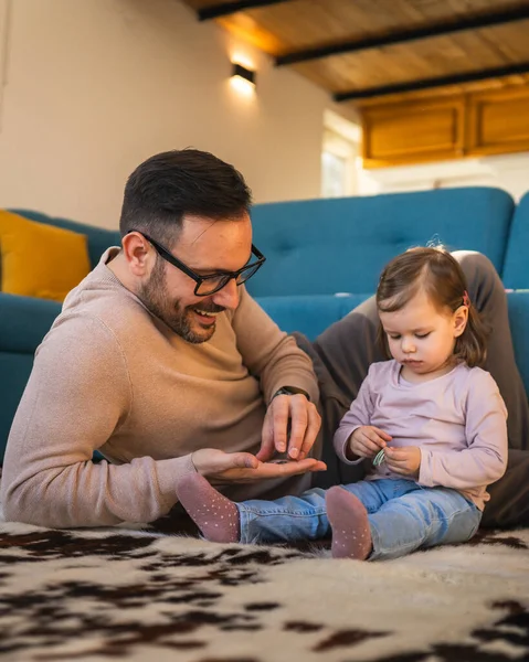 Baba ve kızı evde yerde oynuyorlar olgun yetişkin beyaz adam iki yaşındaki küçük kızıyla oynuyor ebeveynlik yaparak ve aile zamanı konseptini kopyalayarak eğleniyor gerçek insanları taklit ediyor.