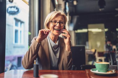 Kafkasyalı bir sarışın kadın kafede ya da restoranda tek başına otururken cep telefonu kullanıyor.