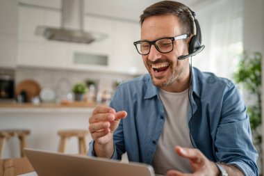 Kafkasyalı bir erkek, evinde kulaklıkla bilgisayar başında müşteri destek, güler yüzlü, güler yüzlü.