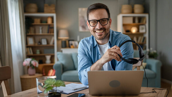 Один человек кавказский мужчина фрилансер работа из дома с наушниками на голове на ноутбуке компьютер поддержки клиентов диспетчер счастливая улыбка уверенно