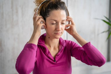 Yetişkin bir beyaz kadın milenyum kulaklıklarını internet rehberli meditasyon için kullanıyor. Evde gözleri kapalı zihin yogası yapıyor. Gerçek insanlar uzay özbakım kavramını taklit ediyorlar.