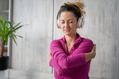 Yetişkin bir beyaz kadın milenyum kulaklıklarını internet rehberli meditasyon için kullanıyor. Evde gözleri kapalı farkındalık yogası yapıyor. Gerçek insanlar uzay sevgisi kavramını taklit ediyorlar.