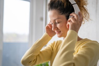 Yetişkin bir beyaz kadın milenyum kulaklıklarını internet rehberli meditasyon için kullanıyor. Evde gözleri kapalı zihin yogası yapıyor. Gerçek insanlar uzay özbakım kavramını taklit ediyorlar.