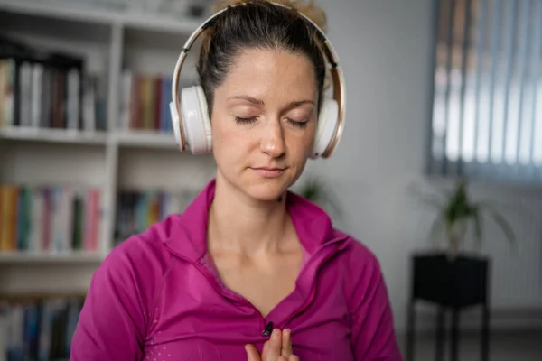 one woman adult caucasian female millennial using headphones for online guided meditation practicing mindfulness yoga with eyes closed on the floor at home real people self-care concept