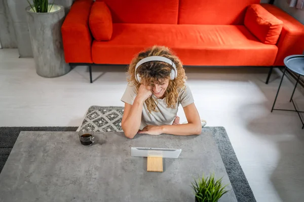 Kıvırcık Saçlı Beyaz Bir Kadın Evde Oturup Dijital Tablet Kulaklık — Stok fotoğraf