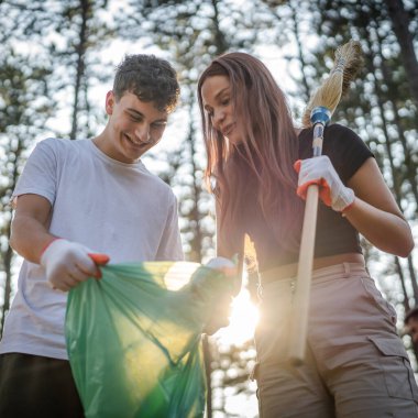 Çift ya da genç arkadaşlar Z erkek ve beyaz kadın atık plastik şişeleri ve kağıtları toplayarak güneşli bir günde çevre koruma kavramının doğasını temizlerler.