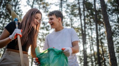 Çift ya da genç arkadaşlar Z erkek ve beyaz kadın atık plastik şişeleri ve kağıtları toplayarak güneşli bir günde çevre koruma kavramının doğasını temizlerler.
