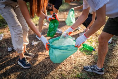 Bir grup arkadaş, Z erkek ve beyaz tenli atık plastik şişe ve kağıt topluyor. Güneşli bir günde çevre koruma kavramının doğasını temizliyor.