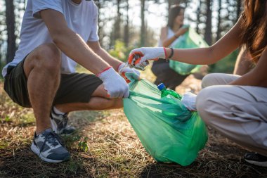 Bir grup arkadaş, Z erkek ve beyaz tenli atık plastik şişe ve kağıt topluyor. Güneşli bir günde çevre koruma kavramının doğasını temizliyor.