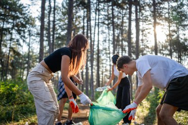 Bir grup genç arkadaş Z erkek ve beyaz kadın atık plastik şişeleri ve kağıtları toplayarak güneşli bir günde çevre koruma kavramının doğasını temizliyorlar.