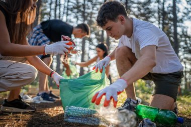 Bir grup genç arkadaş Z erkek ve beyaz kadın atık plastik şişeleri ve kağıtları toplayarak güneşli bir günde çevre koruma kavramının doğasını temizliyorlar.