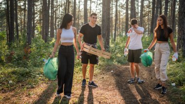 Bir grup genç arkadaş Z erkek ve beyaz kadın atık plastik şişeleri ve kağıtları toplayarak güneşli bir günde çevre koruma kavramının doğasını temizliyorlar.