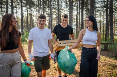 Bir grup genç arkadaş Z erkek ve beyaz kadın atık plastik şişeleri ve kağıtları toplayarak güneşli bir günde çevre koruma kavramının doğasını temizliyorlar.