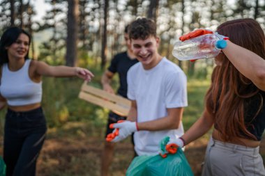 Bir grup genç arkadaş Z erkek ve beyaz kadın atık plastik şişeleri ve kağıtları toplayarak güneşli bir günde çevre koruma kavramının doğasını temizliyorlar.