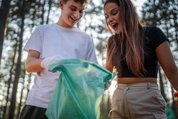 カップルやティーンエイジャーの友人 遺伝子 男性と女性の慎重な男性 ゴミのプラスチックボトルを拾う女性 森林から紙 晴れた日の環境ケアのエコロジーの概念で自然をきれいにする — ストック写真