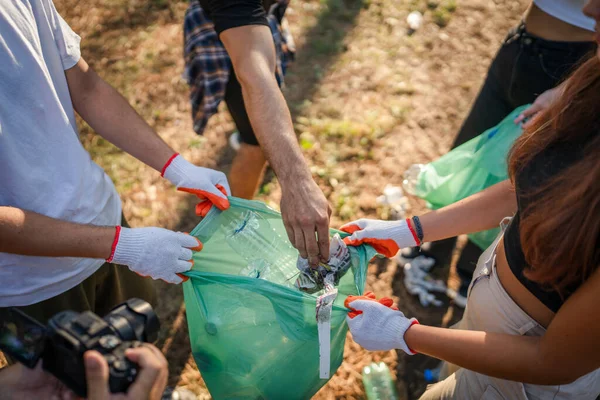 Bir grup arkadaş, Z erkek ve beyaz tenli atık plastik şişe ve kağıt topluyor. Güneşli bir günde çevre koruma kavramının doğasını temizliyor.