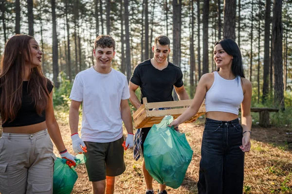 ティーンエイジャーの友人のグループ 男性と女性の慎重な男性 ゴミ捨てプラスチックボトルと森から紙を拾う女性 晴れた日の環境ケアのエコロジーの概念で自然をきれいにする — ストック写真